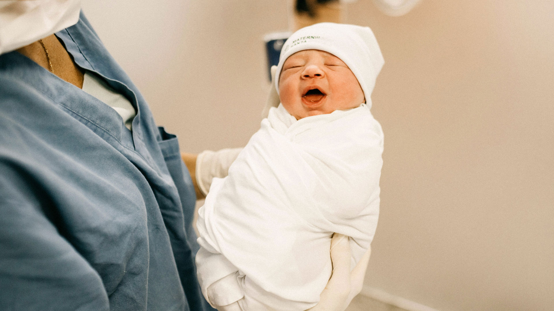 Newborn baby in a white blanket being held by a parent