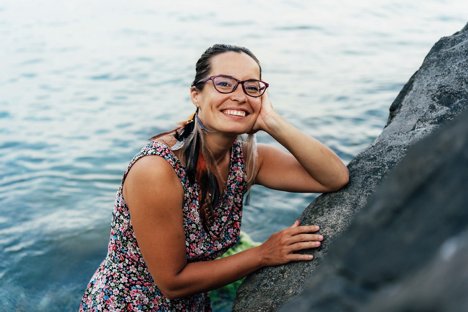 Woman smiling at beach leaning on rock