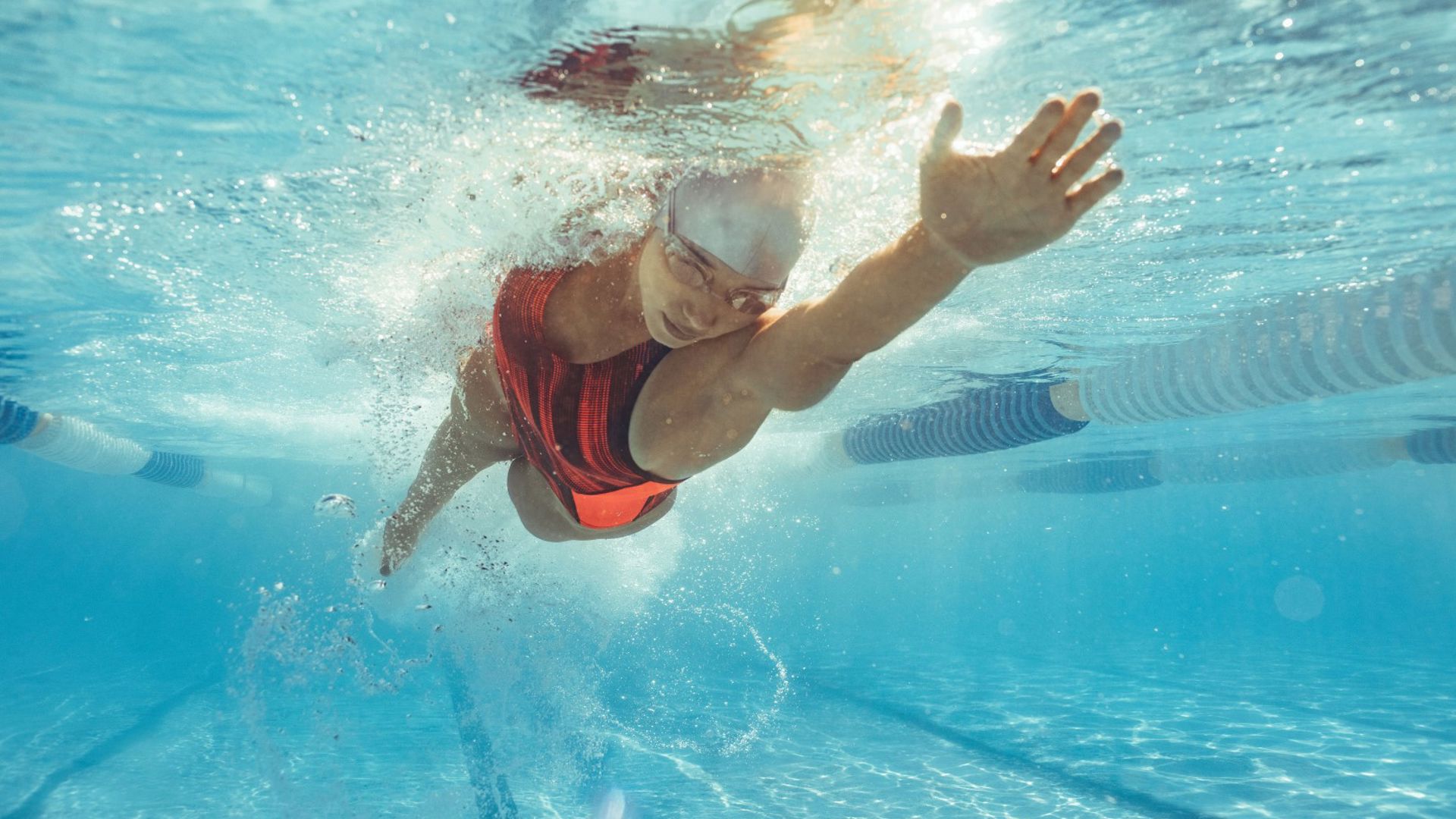 A woman wearing goggles, cap and swimsuit and swimming laps in a pool.