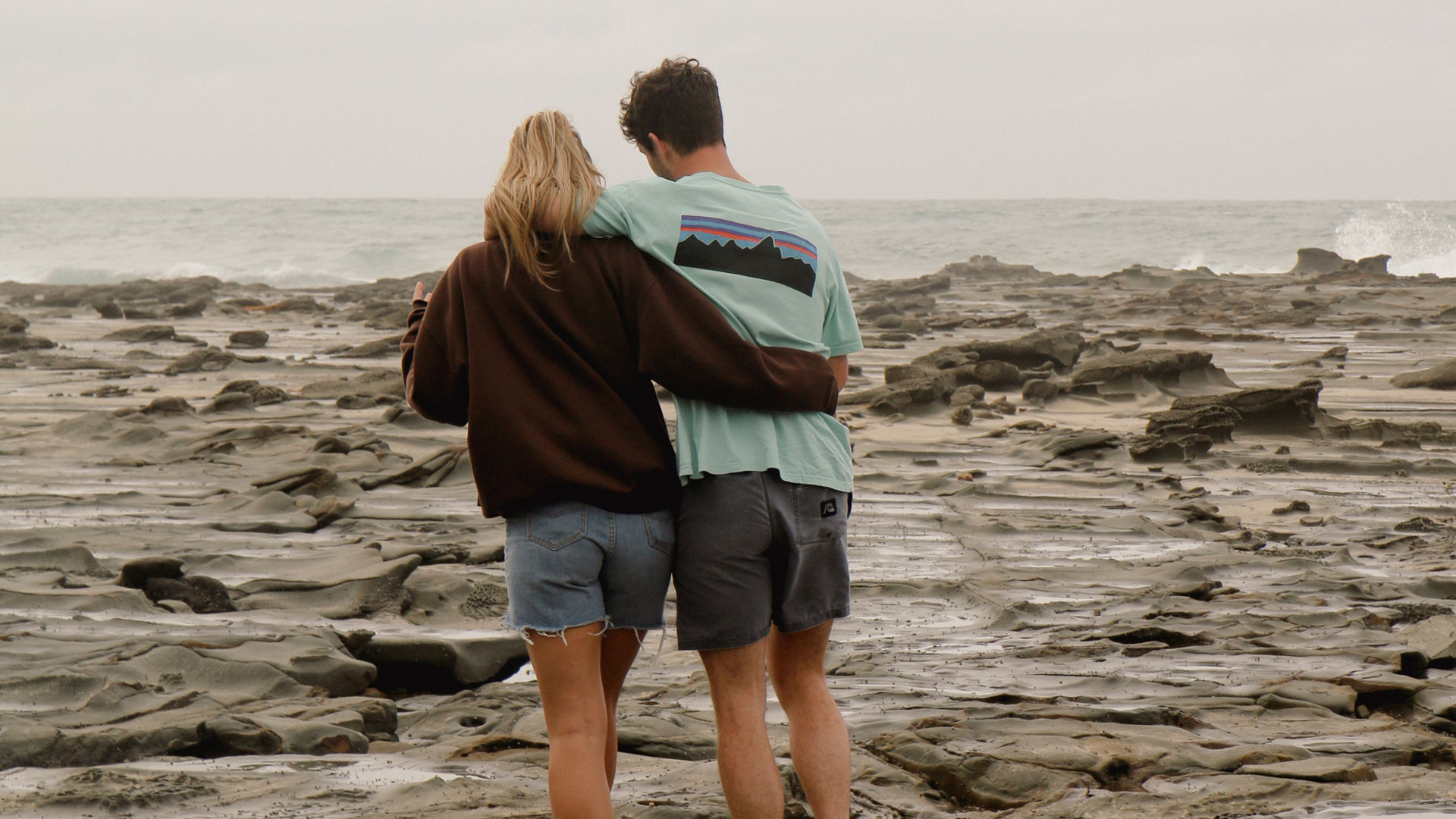 Young couple walking arm in arm together along the beach on the rocks